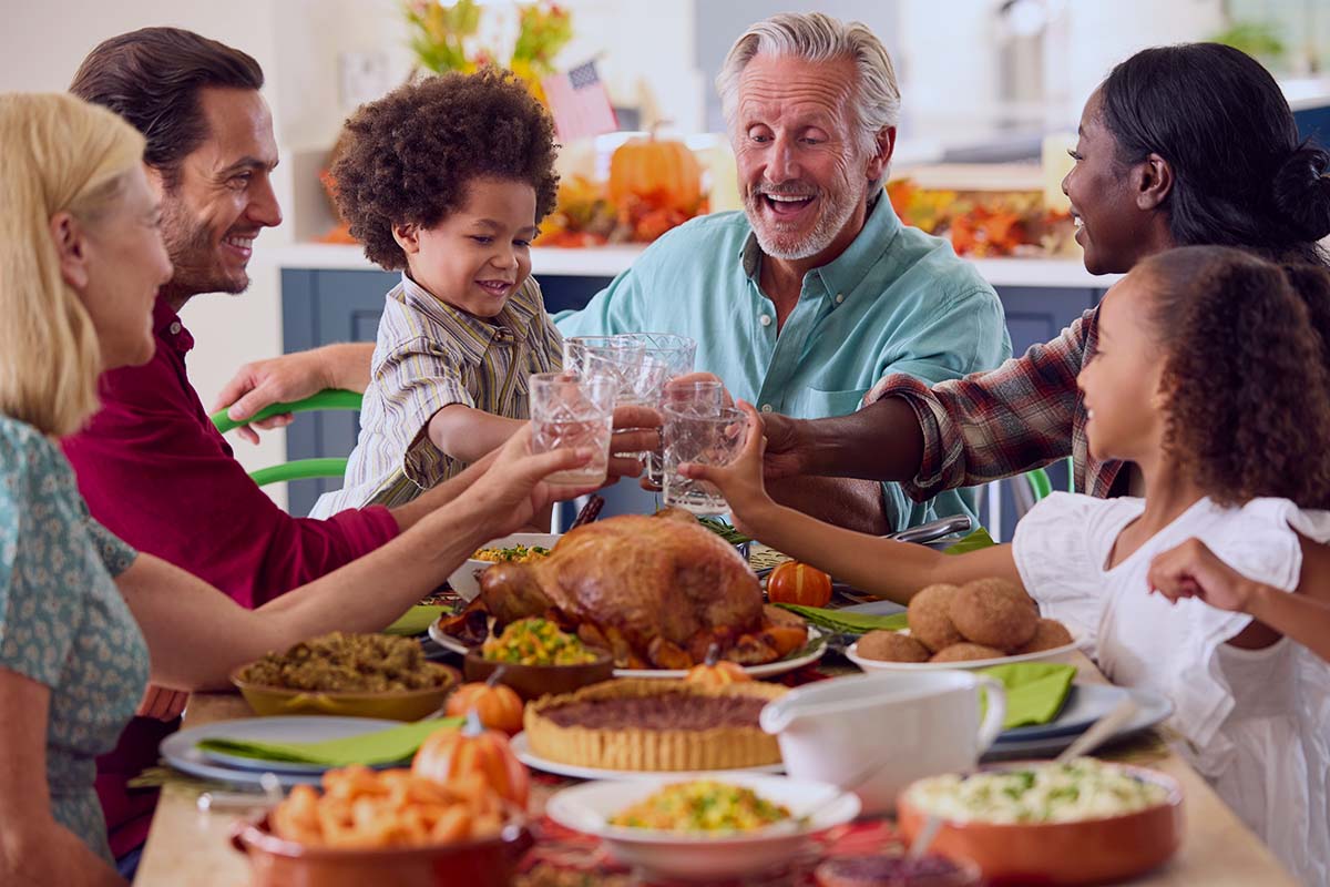 Smiling multi-generational family raising glasses around a Thanksgiving dinner table